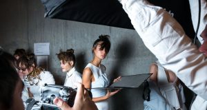 person holding camera taking photo of woman standing near gray wall